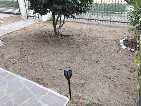 Solar pathway light in a backyard garden bed with bare soil, tree, and fence in background