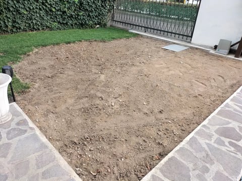 Prepared soil patch in backyard with stone border, metal fence and green grass in background